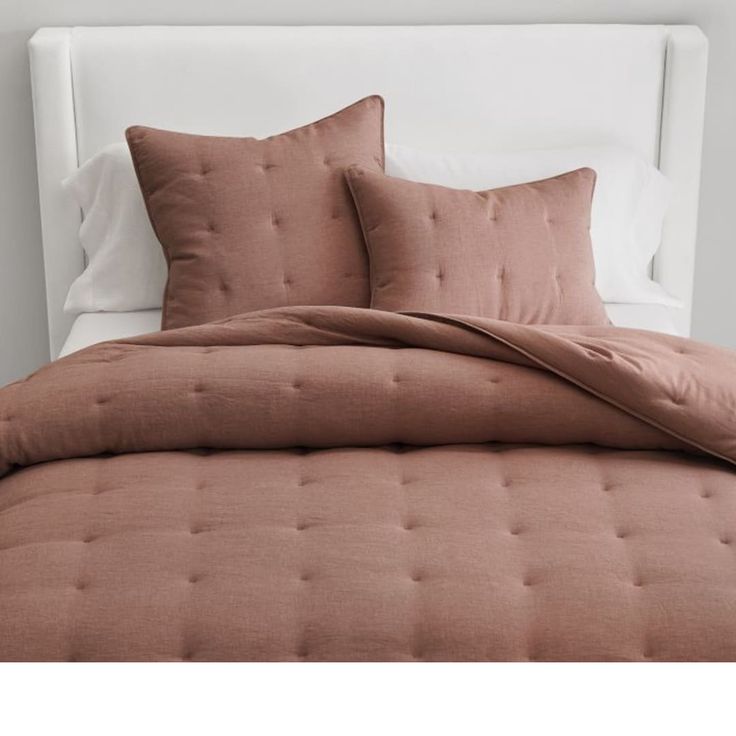 a bed with two pillows on top of it and a white headboard in the background