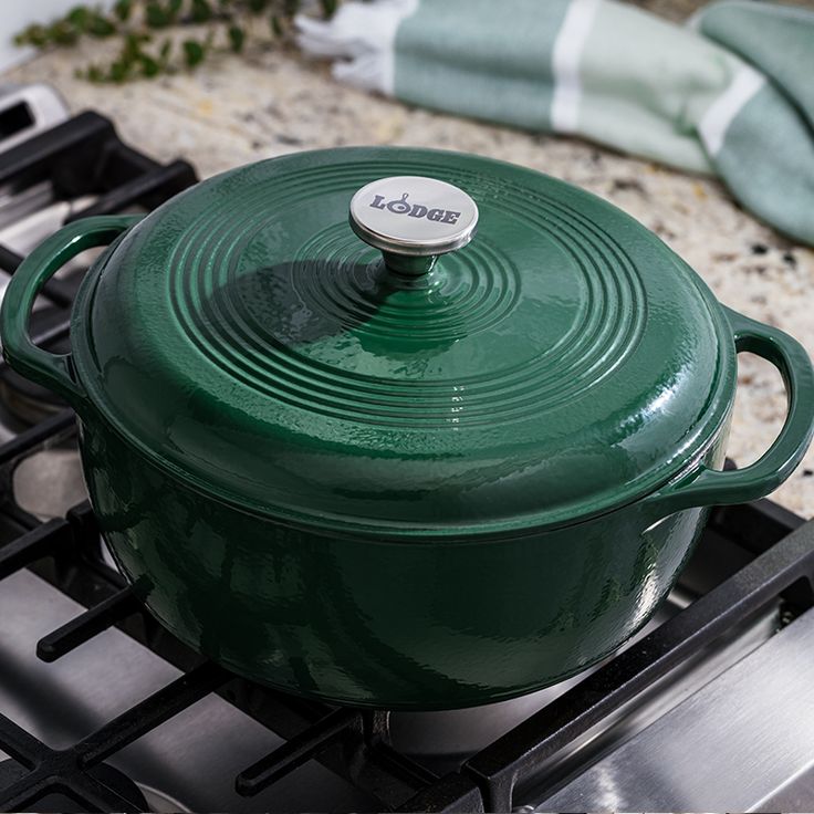 a green casserole sitting on top of a stove next to a blue towel