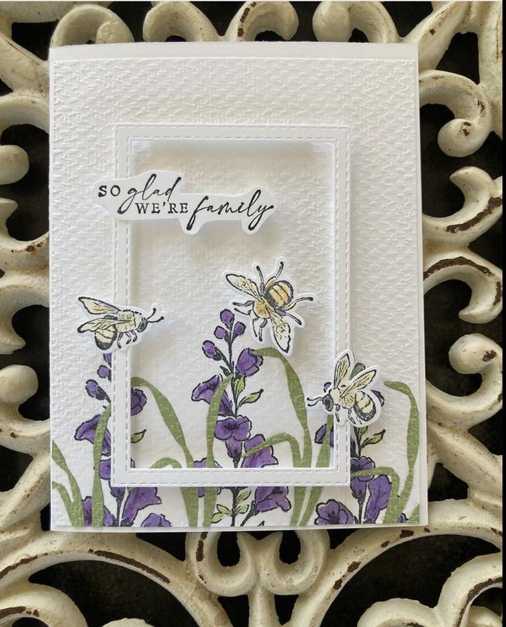 a white card with purple flowers and a bee on it, sitting on a table