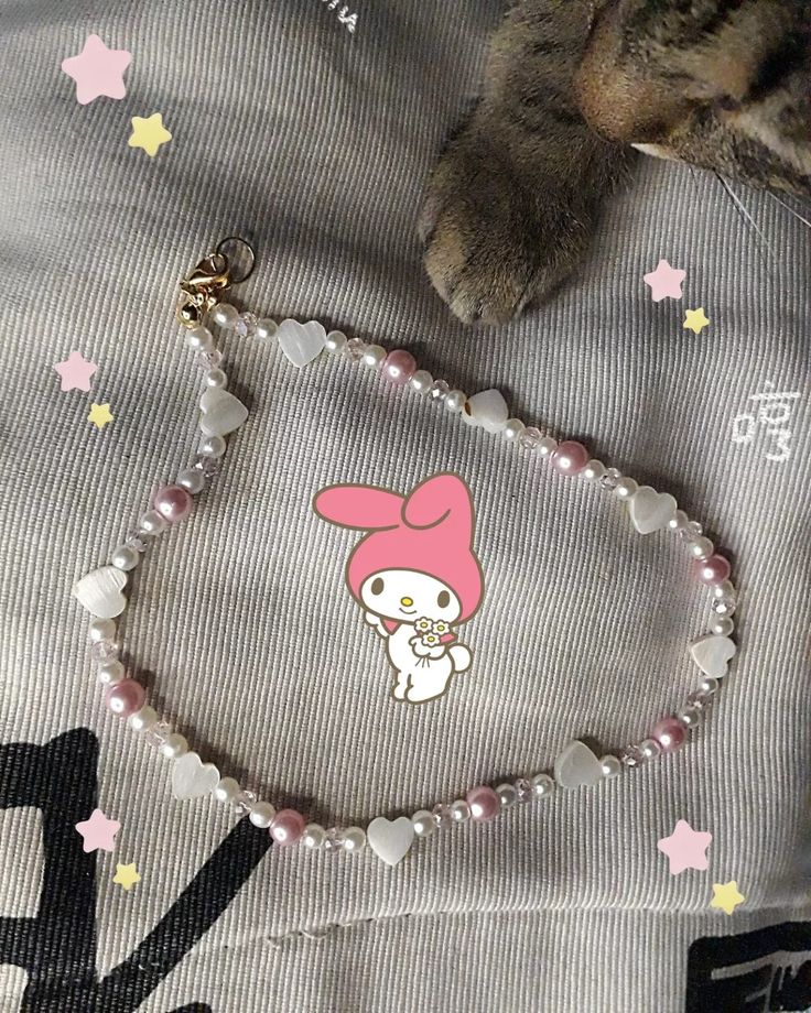 a cat laying on top of a bed next to a necklace with an image of a bunny