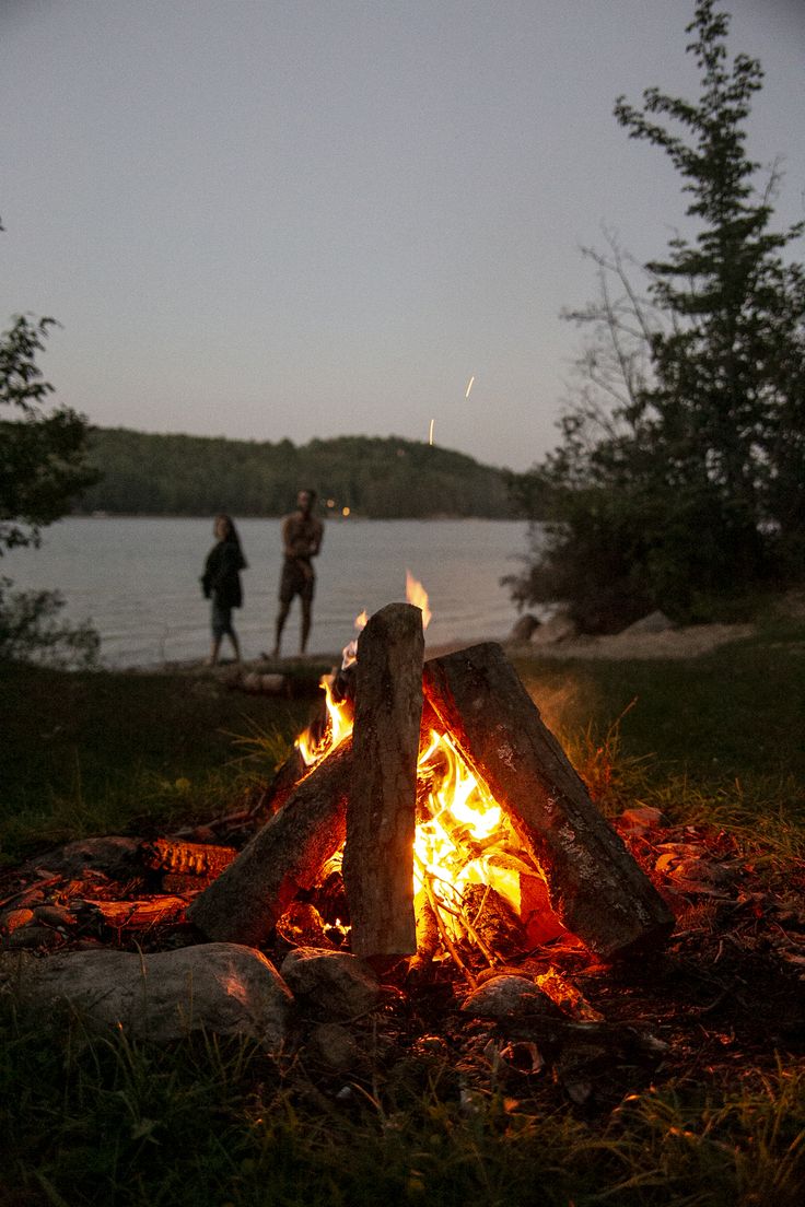 two people standing next to a campfire