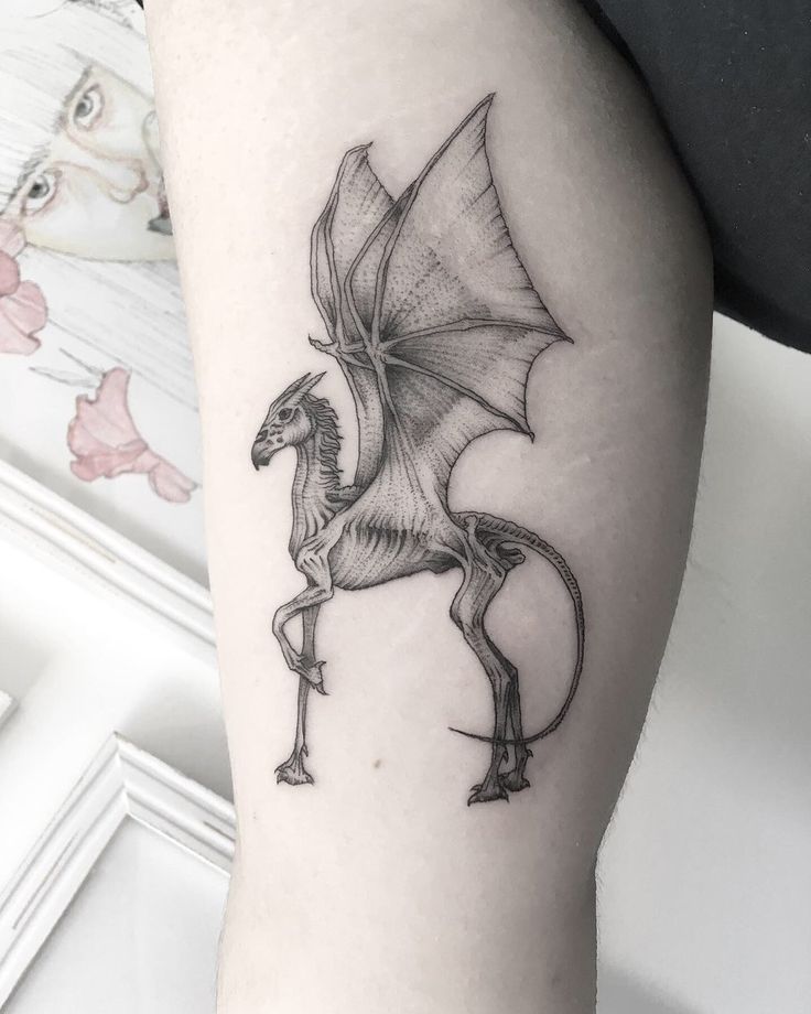 a black and white photo of a dragon tattoo on the right thigh, with wings spread out