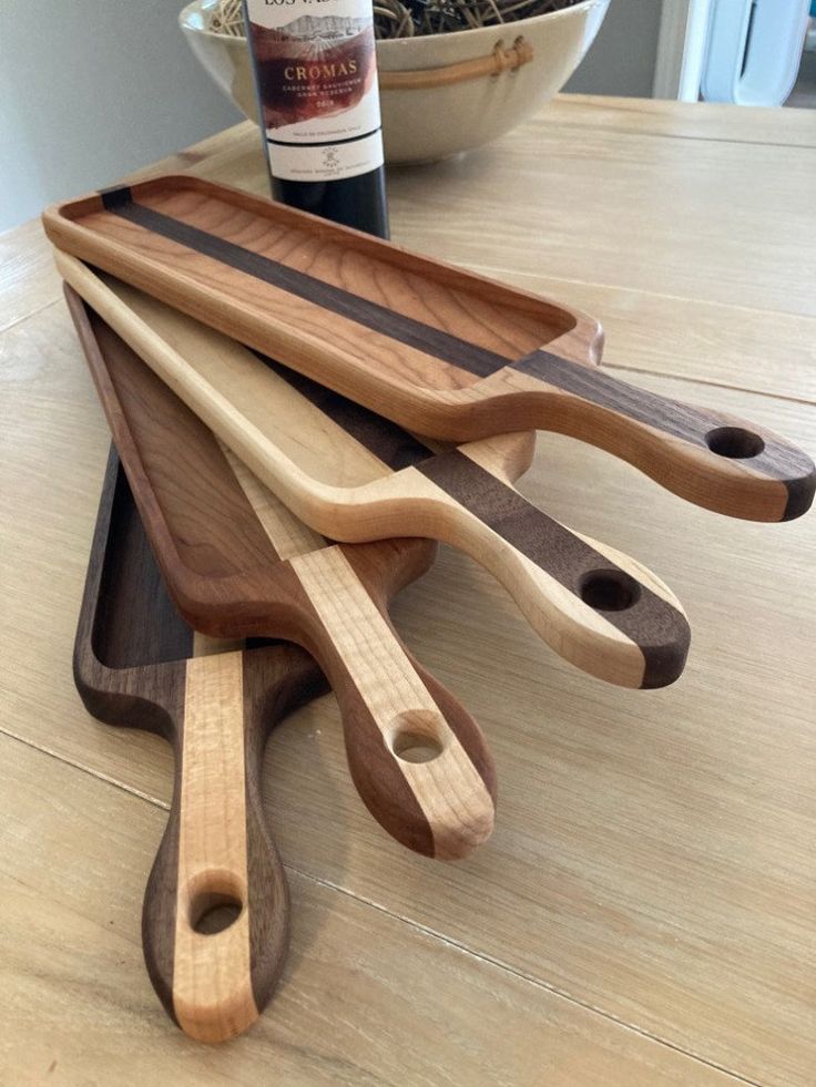 three wooden utensils and a bottle of wine on a table with a bowl in the background