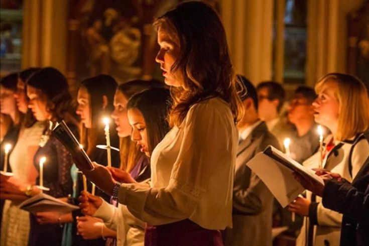 a group of people standing around each other holding candles in their hands and reading books