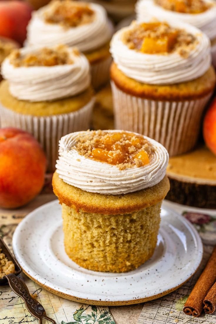 cupcakes with white frosting sitting on a plate next to an apple and cinnamon stick