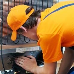 a man in an orange shirt and yellow hat checking the air conditioner