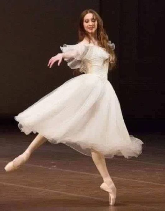 a woman in a white dress is dancing on a stage with her arms outstretched and legs spread out