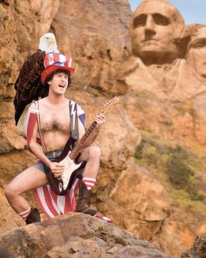 a man with an american flag hat is playing the guitar in front of some carved heads