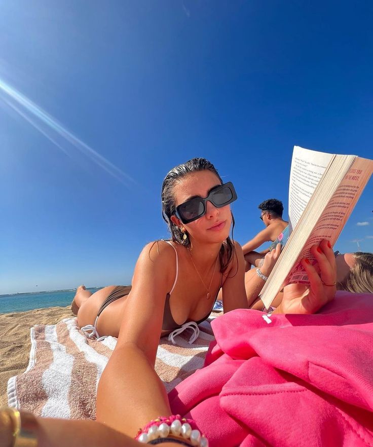 a woman laying on the beach reading a book