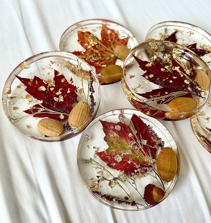 four glass dishes with leaves and nuts in them on a white tableclothed surface