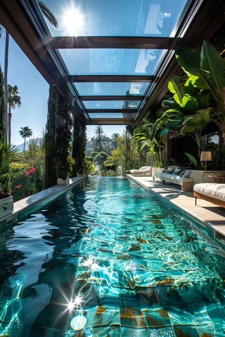 an indoor swimming pool surrounded by greenery and sun shining through the glass roofing