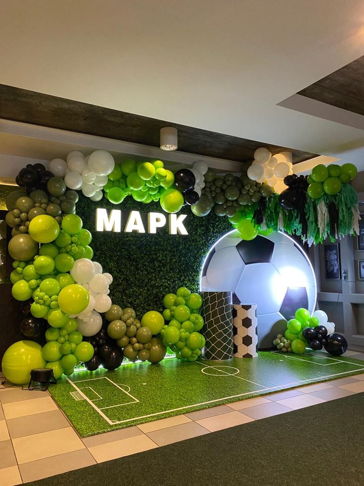 an indoor soccer themed party with balloons and greenery on the wall, along with football field