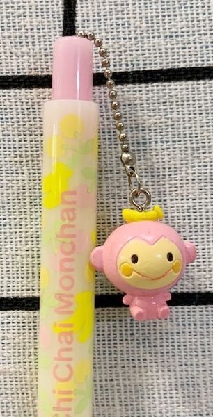 a pink pen with a monkey keychain attached to it's end next to a tube