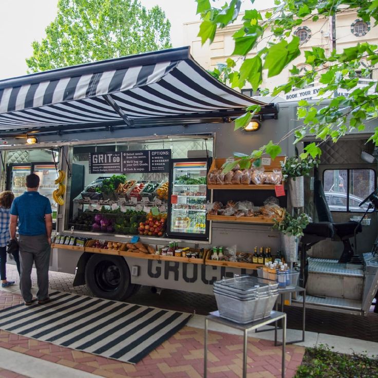 an outdoor food truck with people standing around and looking at it's display on the sidewalk