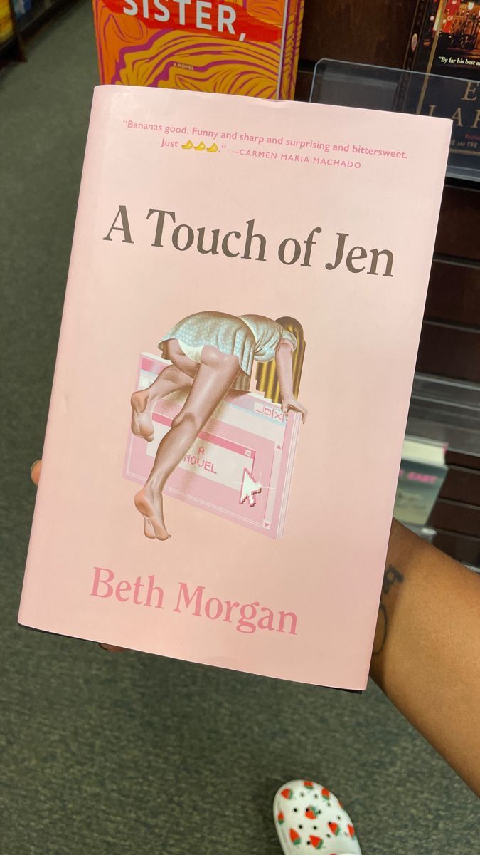 a person holding up a pink book in front of bookshelves on the floor