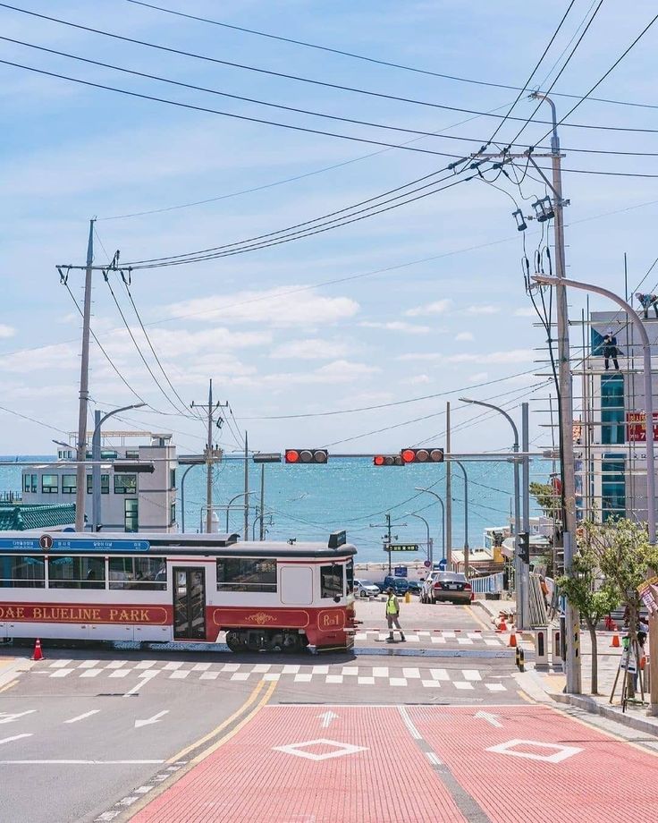 a red and white bus driving down a street next to the ocean on a sunny day