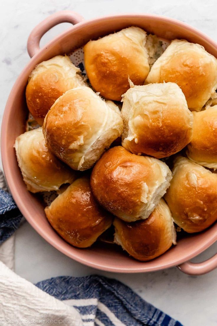 a pink bowl filled with rolls on top of a table