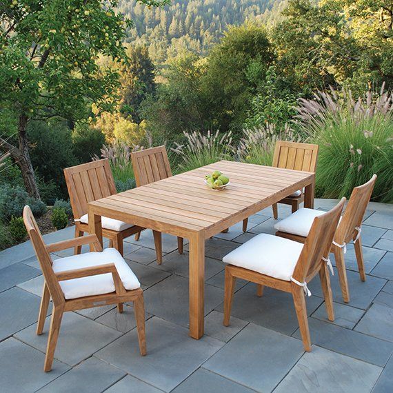 a wooden table and chairs on a patio with plants in the backgroung