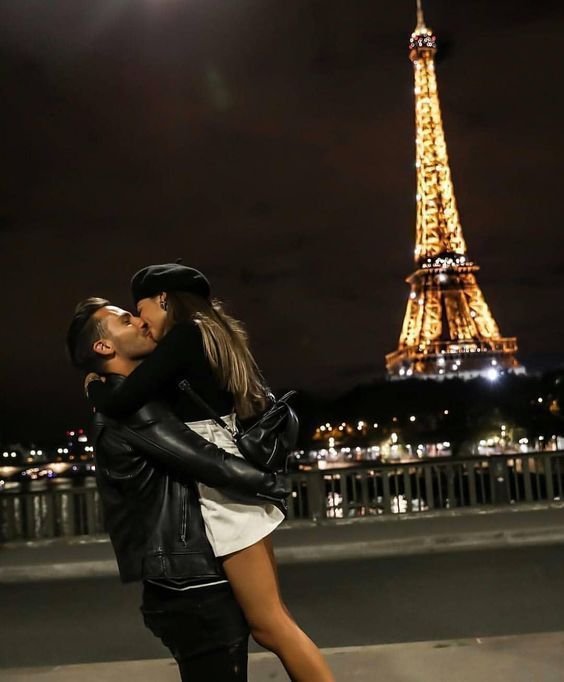 a man and woman kissing in front of the eiffel tower at night time