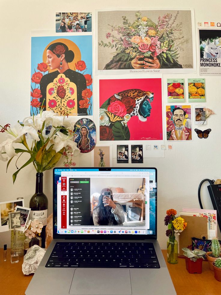 a laptop computer sitting on top of a wooden desk next to a vase filled with flowers