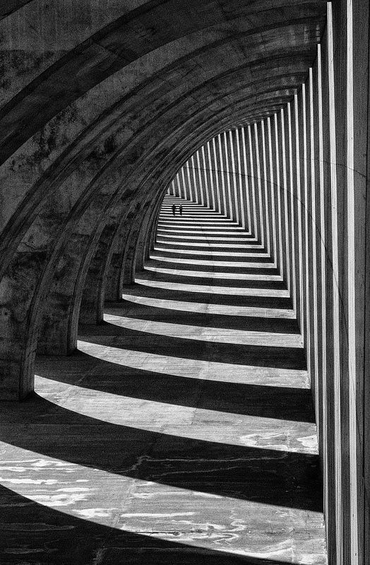 black and white photograph of an arch in a concrete structure with long shadows on the floor