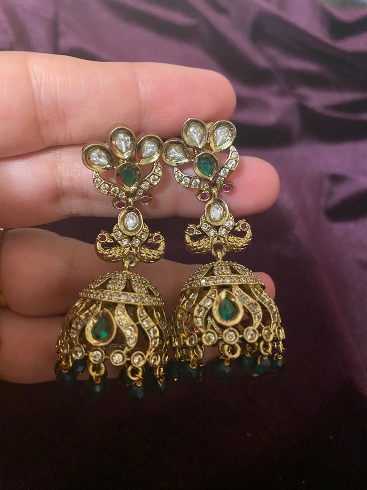 These stunning CZ Green stone Bronze finish AD Jhumkis perfectly complement any Indian outfit. The intricate design and high-quality materials make them a must-have accessory. With a bronze finish and sparkling CZ stones, they add a touch of elegance and sophistication to any look. Length - 5.5cm Jewellery Care- Keep the jewelry dry, avoid heat and contact with perfumes & water. Ornate Jhumkas With Intricate Design For Festivals, Ornate Meenakari Chandbali Jhumkas, Festive Kundan Danglers With Ornate Style, Ornate Kundan Chandbalis With Latkans, Ornate Jhumkas With Latkans, Ornate Jhumkas With Latkans For Festivals, Festive Ornate Kundan Danglers, Brass Meenakari Jhumkas Temple Jewelry, Ornate Kundan Jhumkas