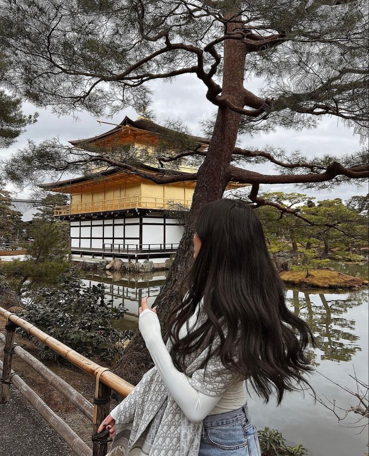 a woman standing in front of a tree looking at a building with a golden roof