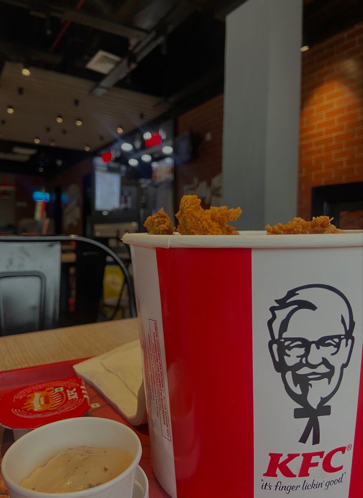 a cup of kfc chicken nuggies next to a bowl of dipping sauce