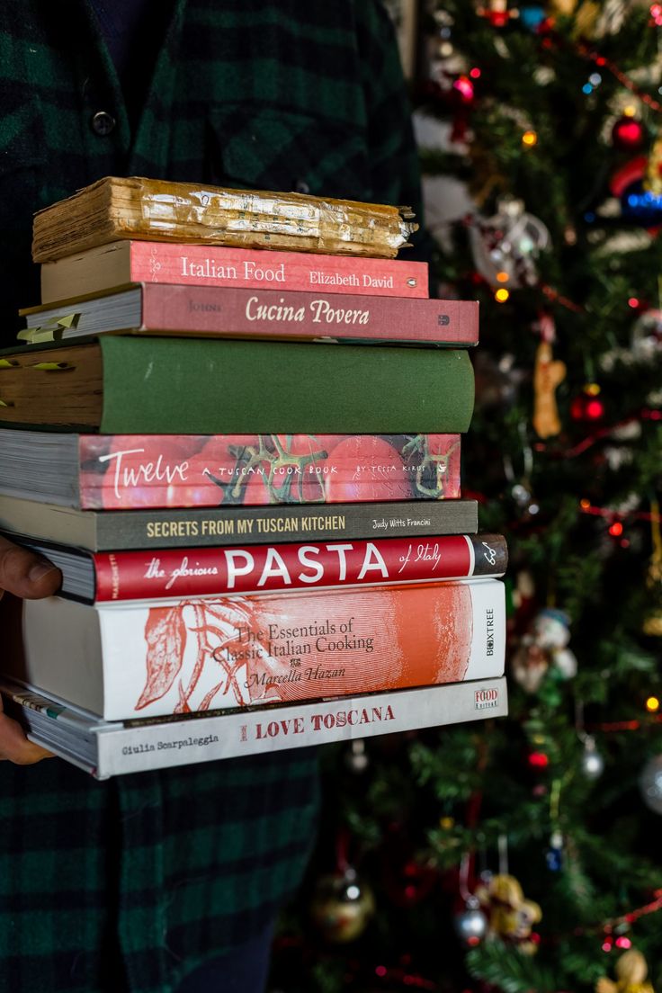 a person holding a stack of books in front of a christmas tree