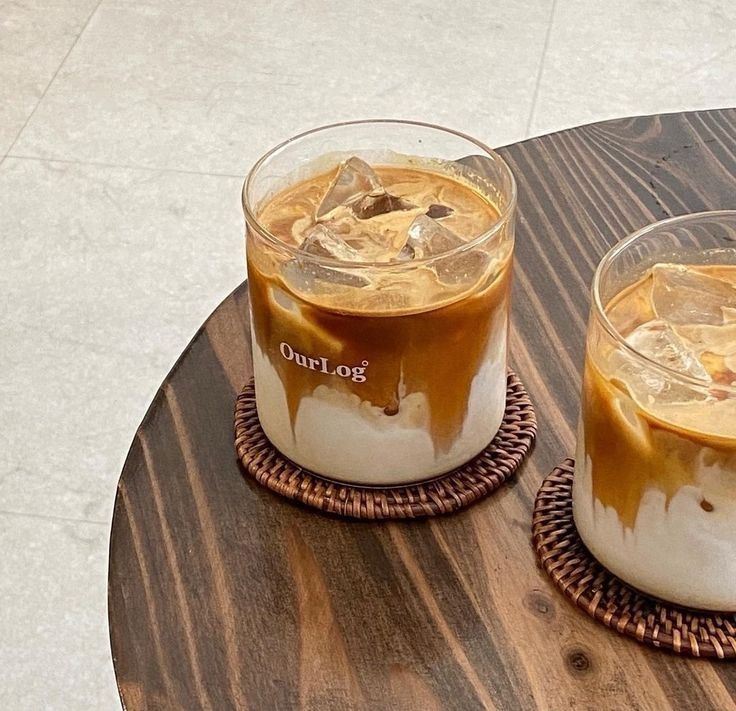 two glasses filled with liquid sitting on top of a wooden table next to each other