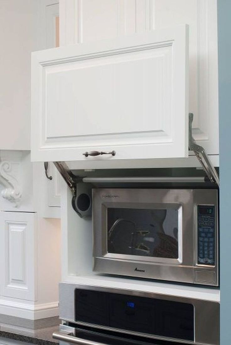 a microwave built into the side of a kitchen wall with white cupboards and drawers