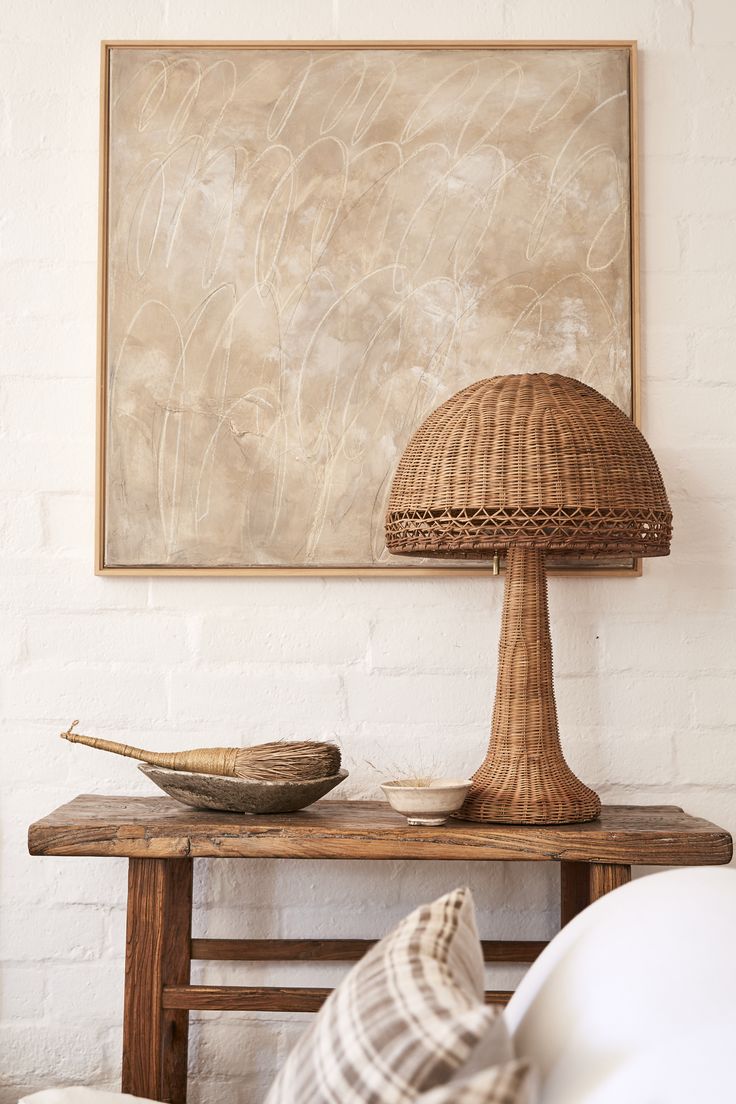 a wooden table topped with a lamp next to a white brick wall and a painting on the wall