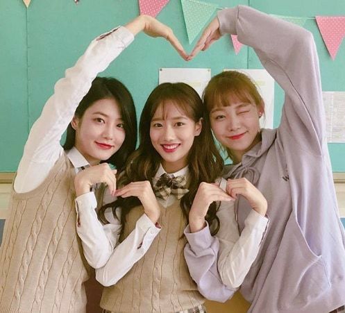 three young women standing next to each other holding their hands in the shape of a heart