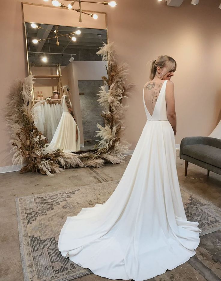 a woman standing in front of a mirror wearing a wedding dress with an open back