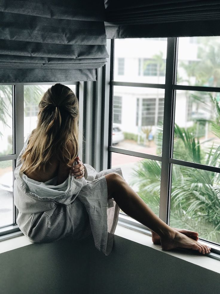 a woman sitting on a window sill looking out at the street and palm trees