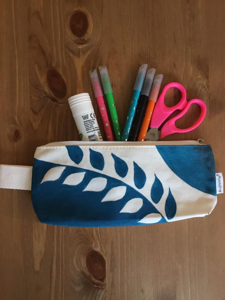 a pencil case filled with markers, pens and scissors on top of a wooden table