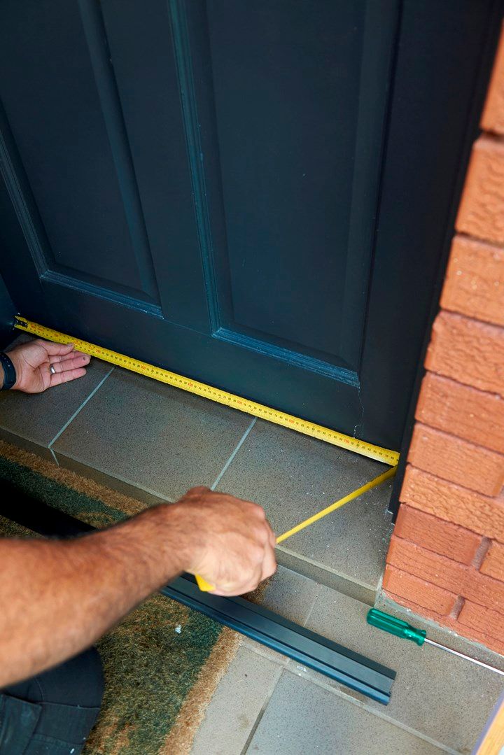 a man measuring the width of a door with a tape measure on his knee and hand