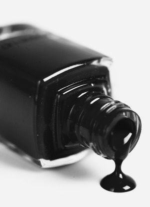 a bottle of black nail polish sitting on top of a white table next to a cup