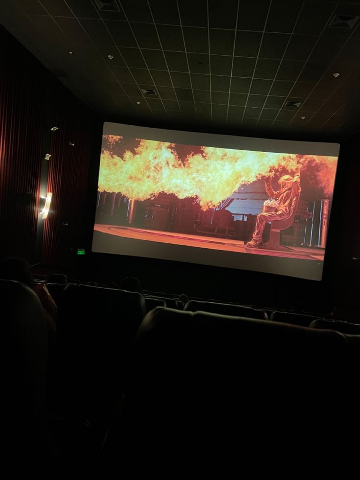 a large screen in the middle of a dark room with people sitting on chairs watching it