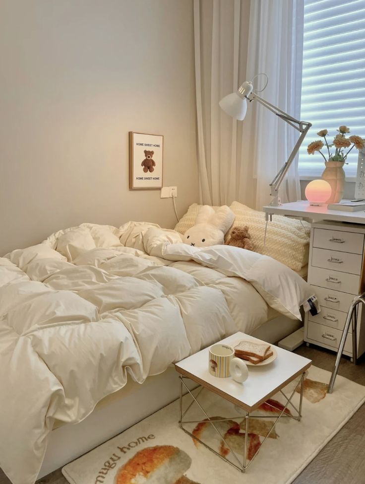 a white bed sitting in a bedroom next to a table with a lamp on top of it