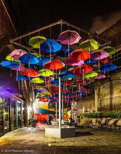 many colorful umbrellas are hanging from the ceiling in an outdoor restaurant area at night