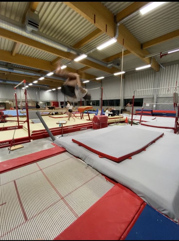 a man is jumping on a trampoline in an indoor gym with red and blue mats