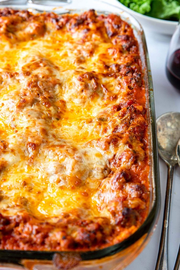 a casserole dish with cheese and meat in it on a table next to silverware