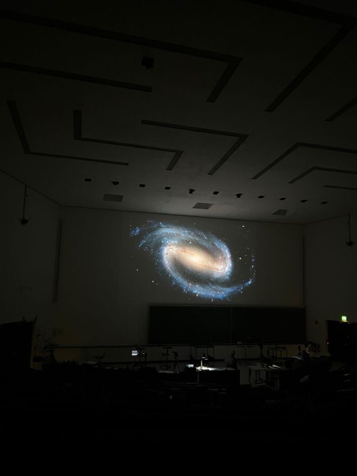 a large screen in the middle of a dark room with lights on it and an image of a spiral galaxy