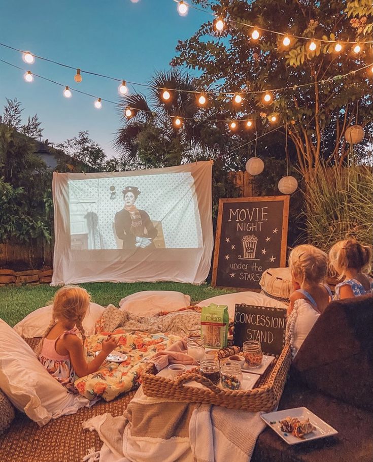 children sitting on the grass watching a movie in front of an outdoor projector screen