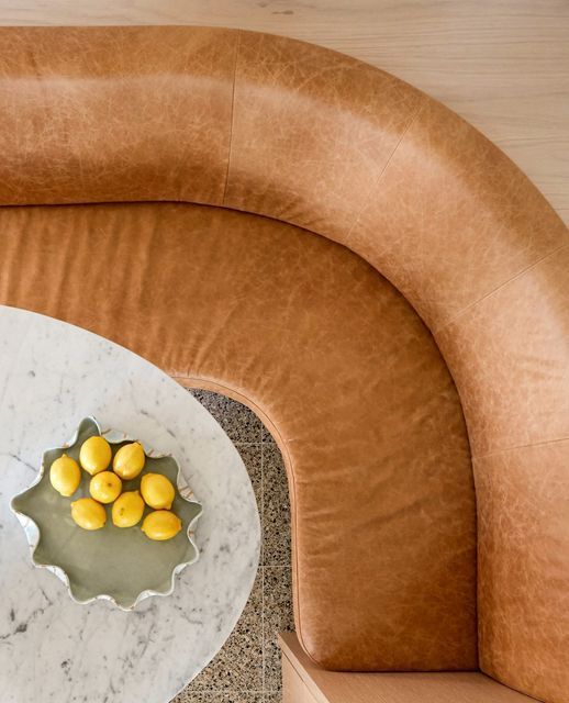 a marble table with yellow fruit on it in the middle of a curved seating area