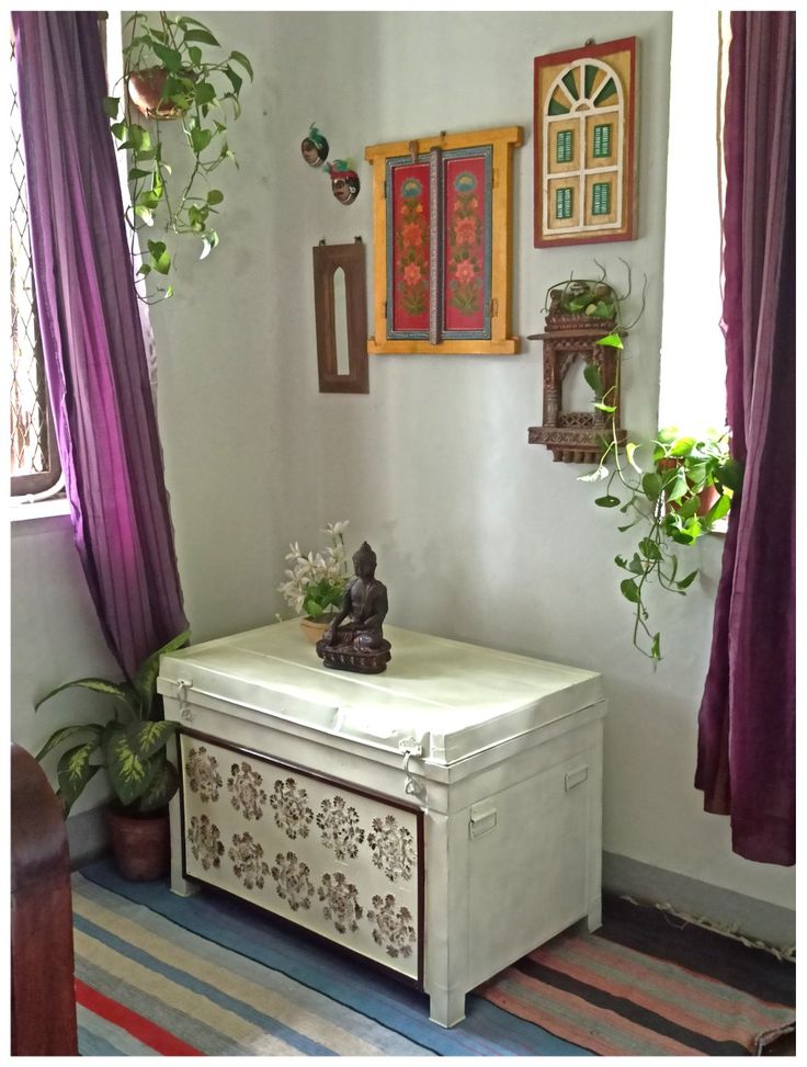 a white chest sitting in the corner of a room with purple curtains and potted plants