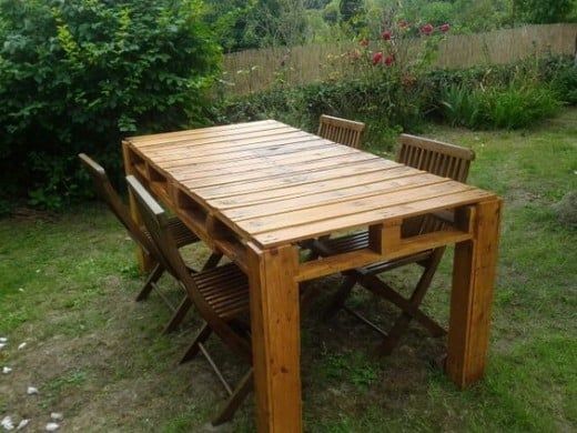 a wooden table and chairs sitting on top of a grass covered field next to bushes