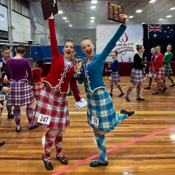 two girls in kilts are holding up their trophy and posing for the camera with other cheerleaders