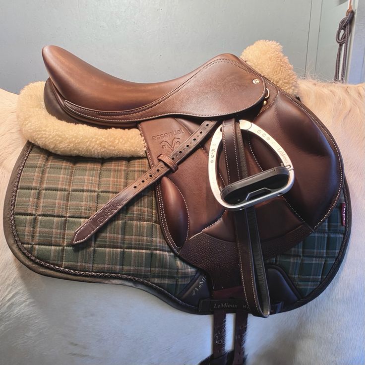 a saddle on top of a white horse with a brown and green plaid blanket around it